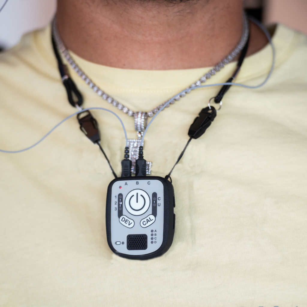A close-up of a person wearing a silver chain necklace with a black and silver wireless control device hanging at the center of the chest.