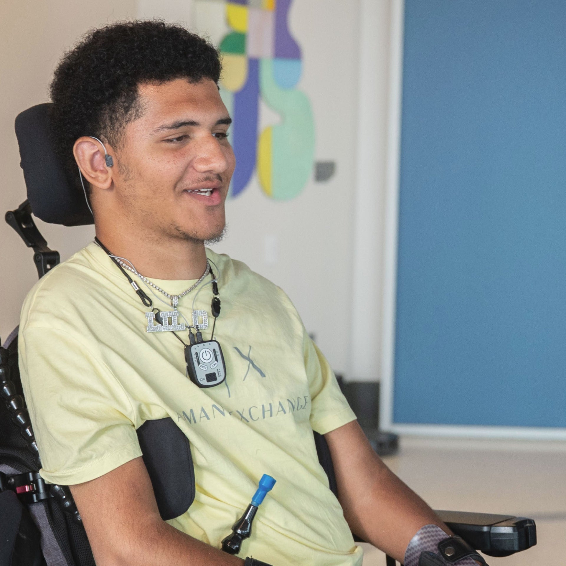 A man in a wheelchair in the center smiles while wearing a pale yellow shirt