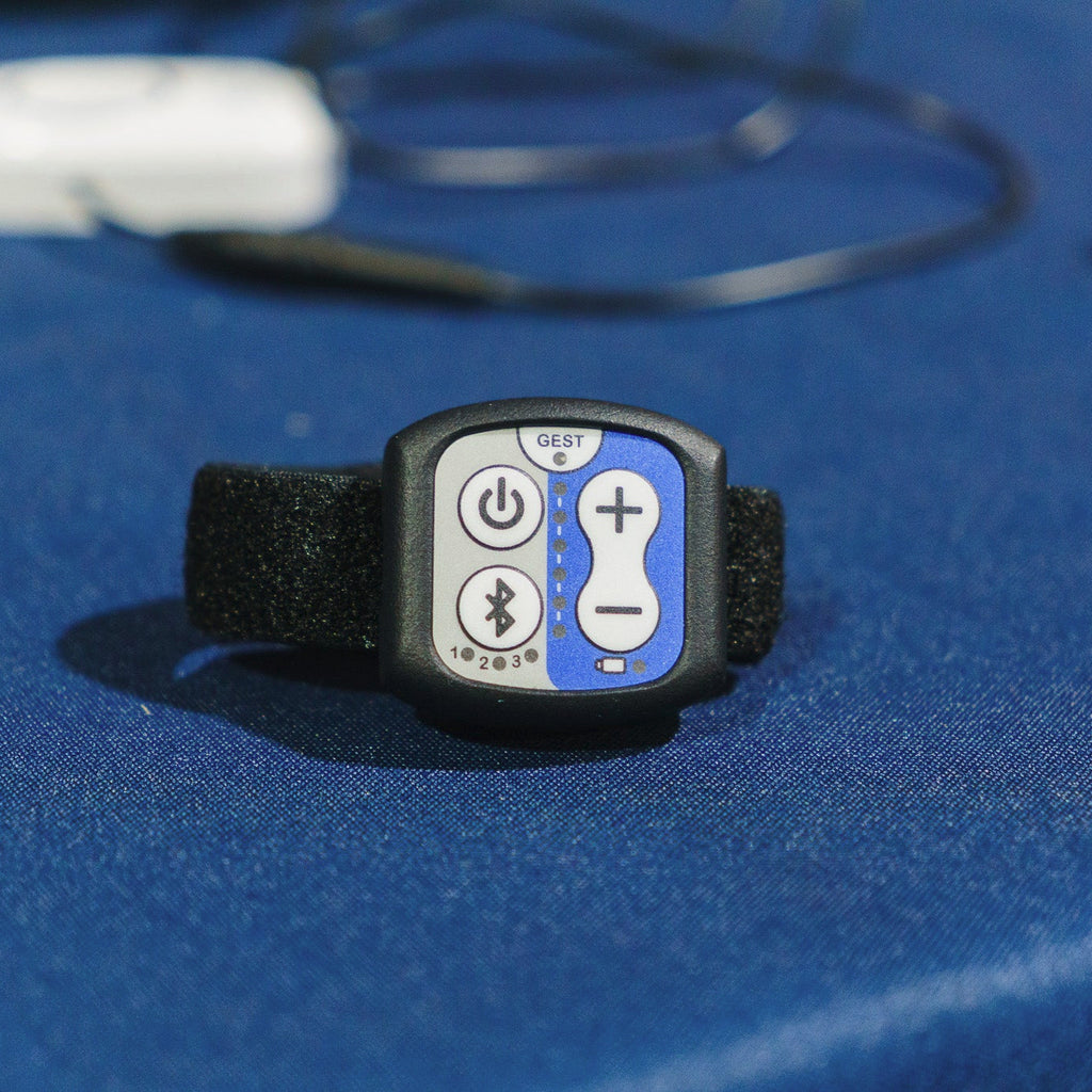 A small electronic control device with a black strap and a faceplate showing power, Bluetooth, plus, and minus buttons on a blue textured surface.