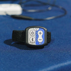 A small electronic control device with a black strap and a faceplate showing power, Bluetooth, plus, and minus buttons on a blue textured surface.