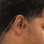 A close-up side profile of a man wearing a Kinemo tracer placed next to his ear with a thin wire extending from the tracer to his neck.