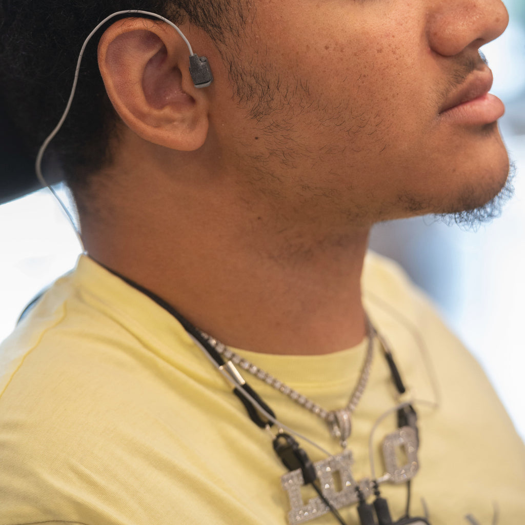 gray wire wrapped around the ear of a person in a light yellow t-shirt.